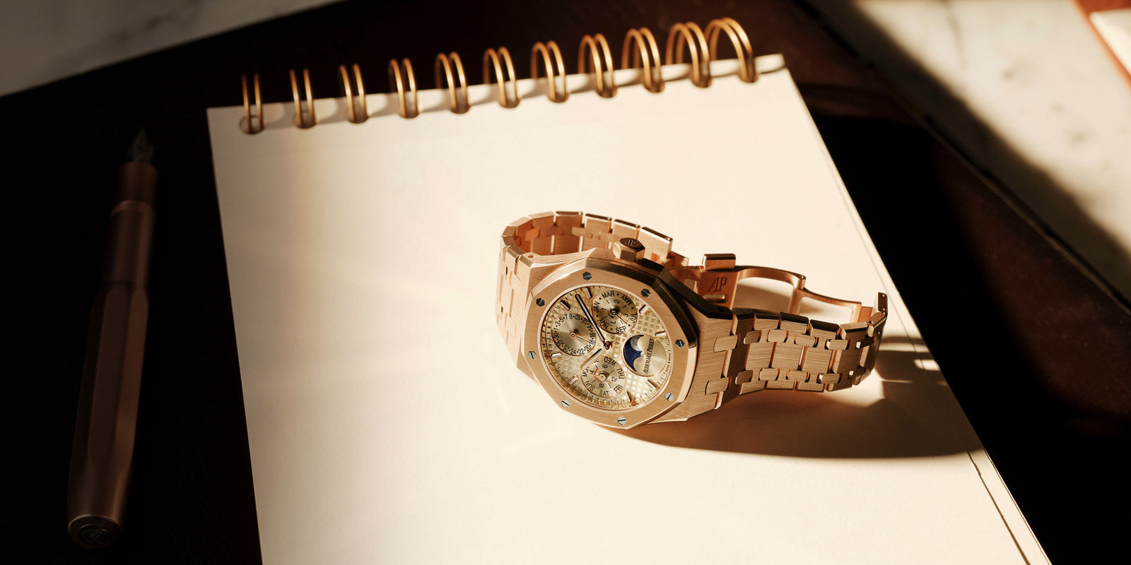 Rose gold watch on a spiral-bound notebook with a pen