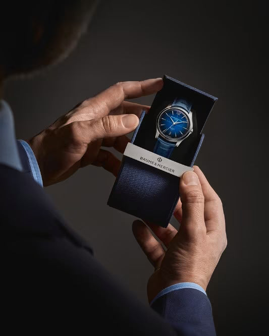 Person holding a blue watch in a dark box against a dark background